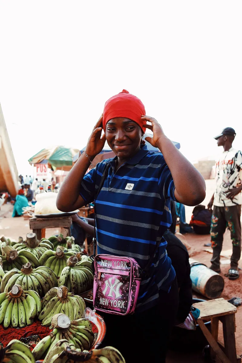 A trader at her market stall, bunches of plantain stacked in front of her
